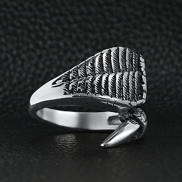 Stainless steel dragon claw and angel wing ring angled on a black leather background.