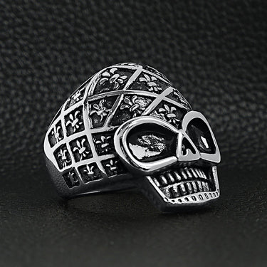 Stainless steel skull with Fleur De Lis pattern ring angled on a black leather background.
