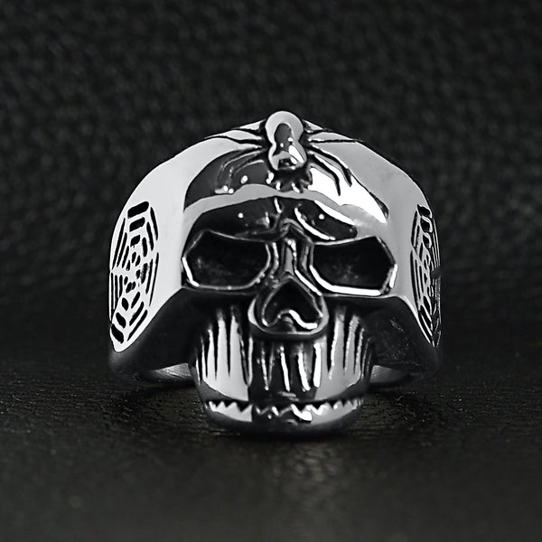 Stainless steel skull with spider and web accents ring on a black leather background.