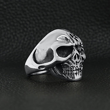 Stainless steel two-faced skull ring angled on a black leather background.