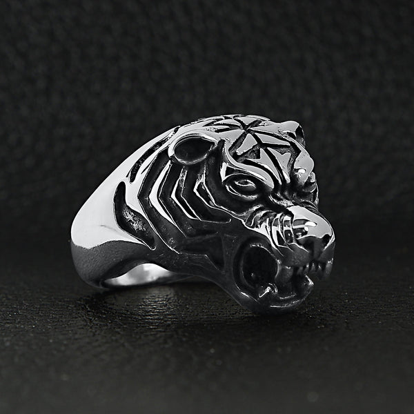 Stainless steel snarling tiger ring angled on a black leather background.