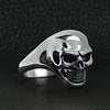Stainless steel skull women's ring angled on a black leather background.