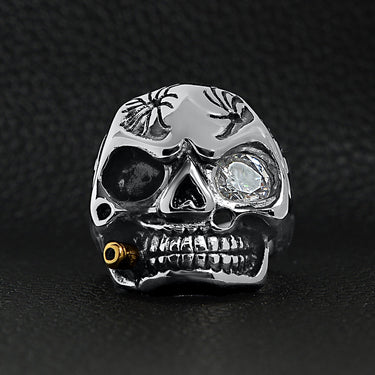 Stainless steel skull smoking 18K gold PVD Coated cigar and single Cubic Zirconia eye ring on a black leather background.