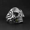 Stainless steel skull smoking 18K gold PVD Coated cigar and single Cubic Zirconia eye ring angled on a black leather background.