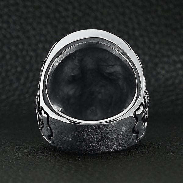 Stainless steel skull with skeleton accents ring back view on a black leather background.
