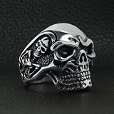 Stainless steel skull with skeleton accents ring angled on a black leather background.