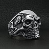 Stainless steel skull with skeleton accents ring angled on a black leather background.