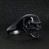 Stainless steel black skull ring angled on a black leather background.