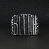 Stainless steel "BITCH" signet ring on a black leather background.