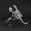 Stainless steel scorpion ring angled on a black leather background.