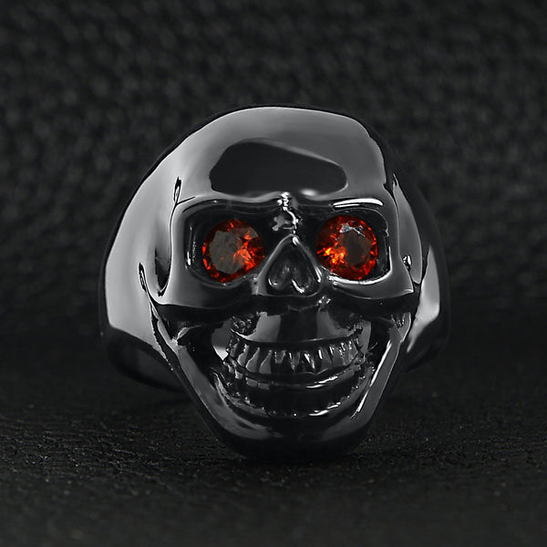 Stainless steel red Cubic Zirconia eyed black skull ring on a black leather background.
