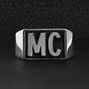Stainless steel motorcycle club "MC" insignia signet ring on a black leather background.