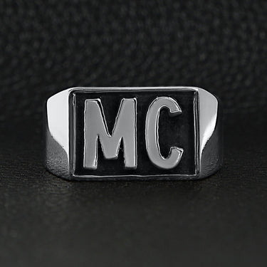 Stainless steel motorcycle club "MC" insignia signet ring on a black leather background.