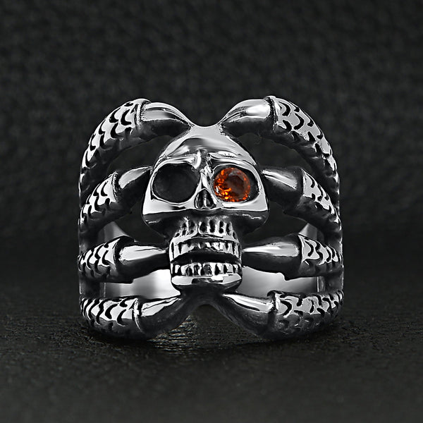 Stainless steel dragon claws holding Red Cubic Zirconia eyed skull ring on a black leather background.