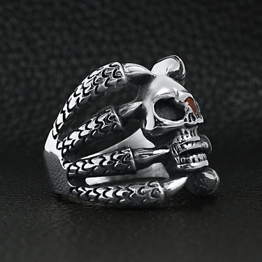 Stainless steel dragon claws holding Red Cubic Zirconia eyed skull ring angled on a black leather background.