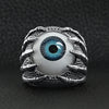 Stainless steel skeleton hands holding blue eyeball ring on a black leather background.