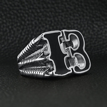 Stainless steel black gothic "13" dragon claw signet ring angled on a black leather background.