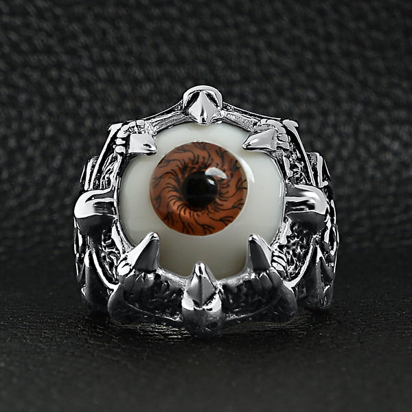 Stainless steel gothic red eyeball with claw and skull accents ring on a black leather background.