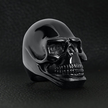 Stainless steel black skull ring angled on a black leather background.