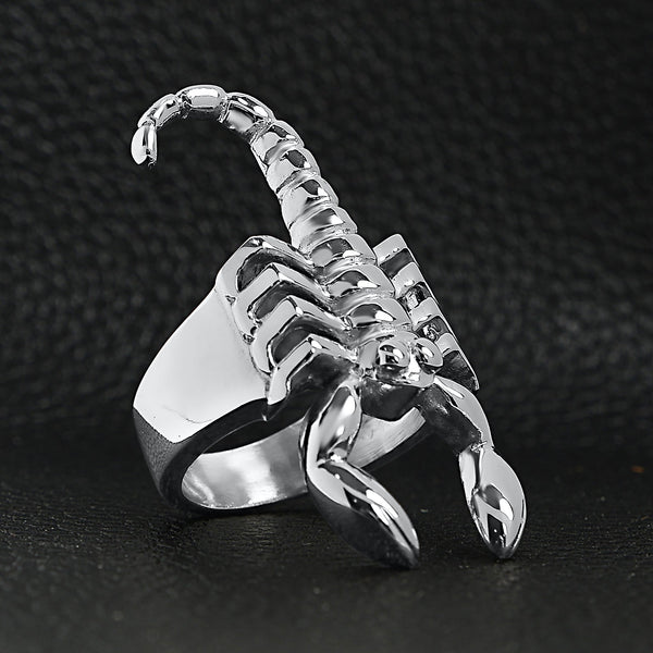 Stainless steel scorpion men's ring angled on a black leather background.