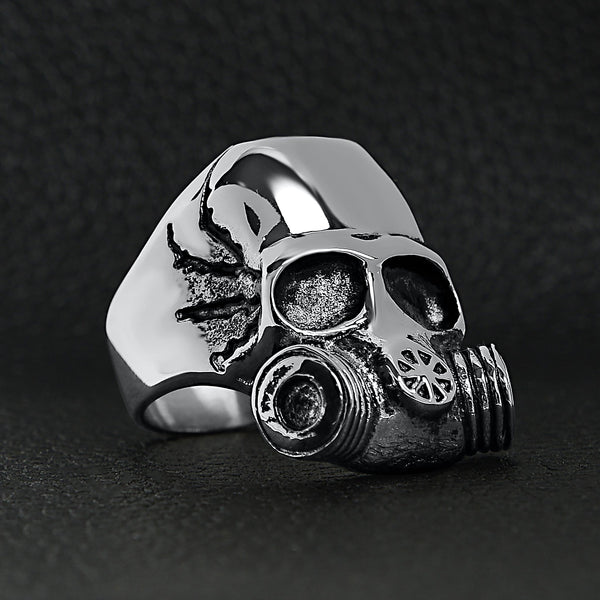 Stainless steel gas mask skull ring angled on a black leather background.