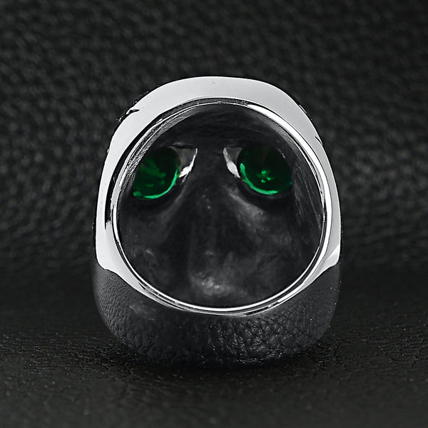 Stainless steel green Cubic Zirconia eyed cracked skull ring back view on a black leather background.