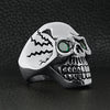 Stainless steel green Cubic Zirconia eyed cracked skull ring angled on a black leather background.