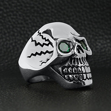 Stainless steel green Cubic Zirconia eyed cracked skull ring angled on a black leather background.