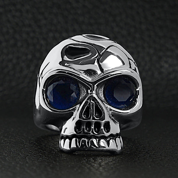 Stainless steel blue Cubic Zirconia eyed cracked skull ring on a black leather background.