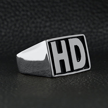 Stainless steel heavy duty "HD" signet ring angled on a black leather background.