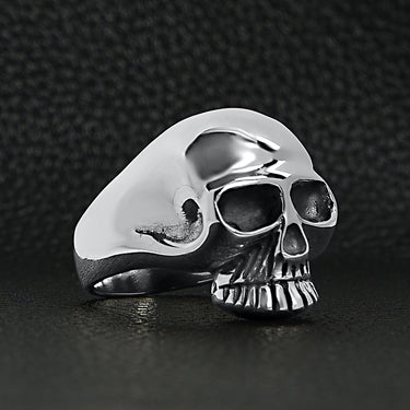Sterling silver skull ring side view on a black leather background.