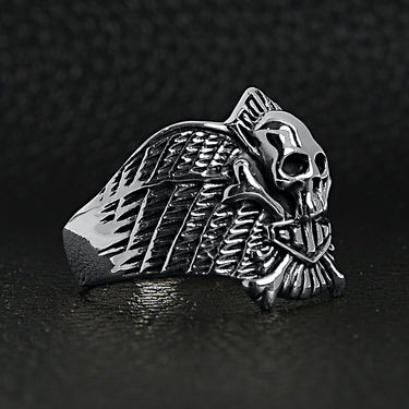 Sterling silver winged skull and crossbones shield ring angled view on a black leather background.