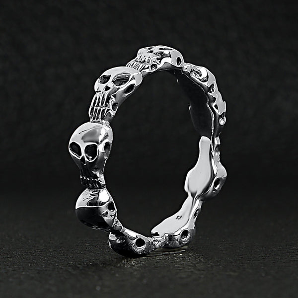 Sterling silver skulls ring standing up on a black leather background.