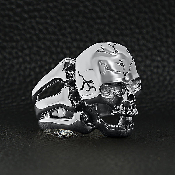 Sterling silver screaming cracked skull with bones ring at an angle on a black leather background.