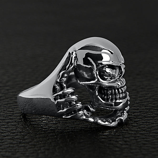 Sterling silver skull tearing through ring angled on a black leather background.
