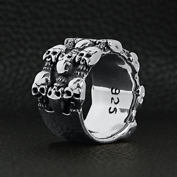 Sterling silver triple layer skulls ring standing up on a black leather background.