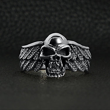 Sterling silver fanged skull with wings ring on a black leather background.