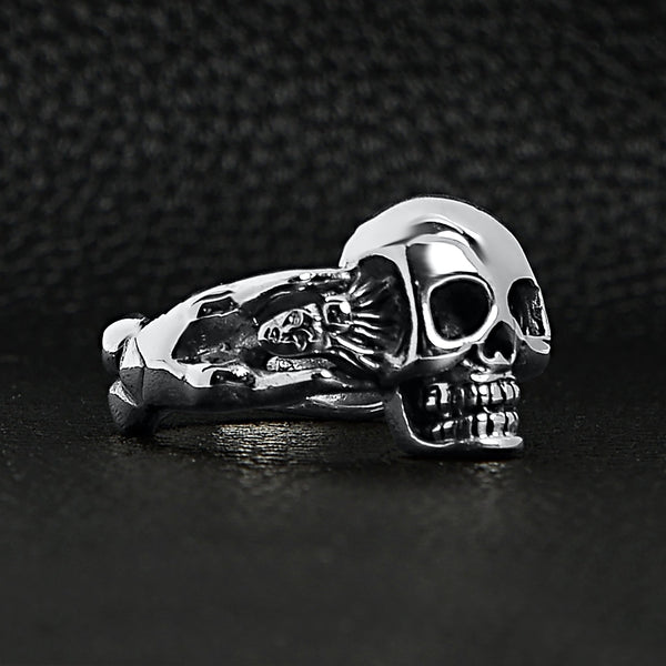 Sterling silver skull and nude women ring angled on a black leather background.
