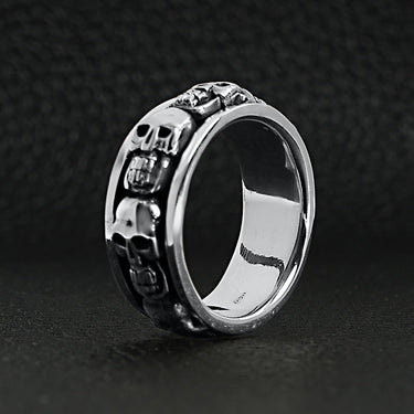 Sterling silver skull spinner ring upright on a black leather background.