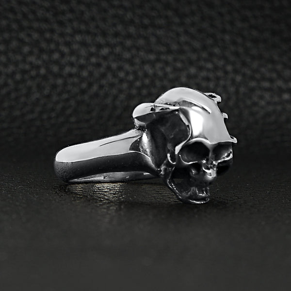 Sterling silver skull in demon hand ring angled on a black leather background.