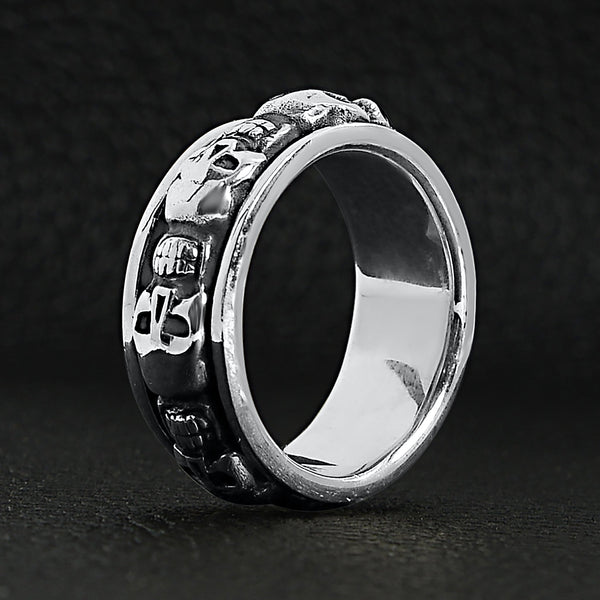 Sterling silver skull spinner ring upright on a black leather background.
