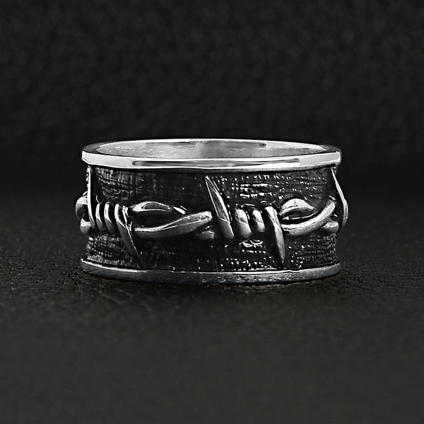 Sterling silver barbed wire ring on a black leather background.